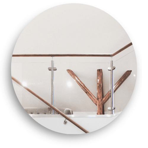 Et indendørs glasværn med rustfri stolper og håndliste i træ. Værnet indrammer et åbent område og tilføjer en varm, naturlig stemning til rummet.