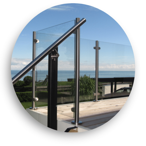 Moderne glasgelænder med rustfri stolper og håndliste, installeret på terrasse med fri udsigt over havet.