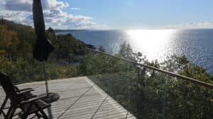 Hjørnemonteret glasværn med træhåndliste og panoramaudsigt over skov og hav fra terrasse.