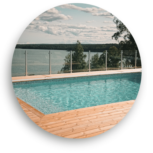 Glashegn med aluminiumsstolper omkring træbeklædt pool, forener sikkerhed med fri udsigt over sølandskab.