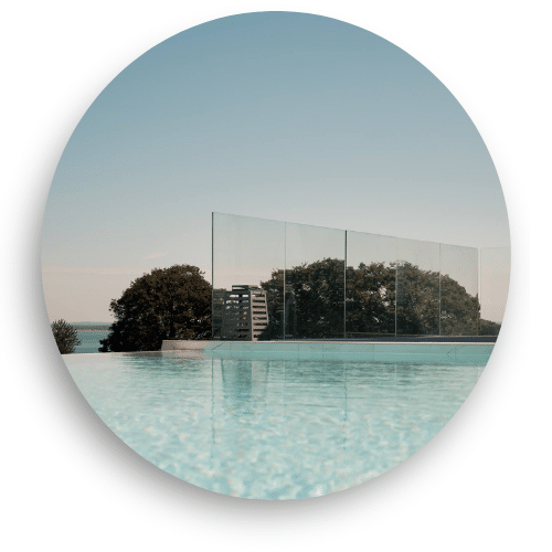 Stolpefrit glasværn ved poolområde med panoramaudsigt over trækroner og hav – elegant glas til terrasse.