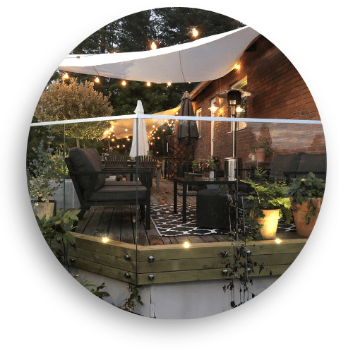 Glasværn i kombination af træ og glas på terrasse med aftenbelysning, lyskæder og havemøbler – oplagt til lukket altan.