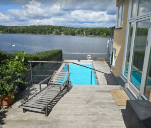 Wiregelænder i rustfrit stål ved moderne pool Wiregelænder i rustfrit stål omkring trætarrasse og pool med søudsigt – diskret og sikkert gelænder til terrasse med niveauforskel.