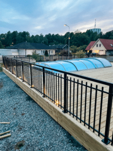 Smedejernsgelænder i sort aluminium ved pool Sortlakeret poolhegn i Alu Retro-design omkring terrasse med træbrædder – klassisk løsning med høj sikkerhed.