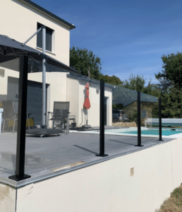 Glashegn i sort aluminium ved hævet pool Sikkert poolhegn i klart lamineret glas med sorte aluminiumsstolper omkring hævet terrasse med moderne udendørsområde.