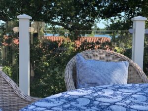 Nærbillede af terrasse med hvidt aluminiumsgelænder, klart glas, rottingmøbler og søudsigt.