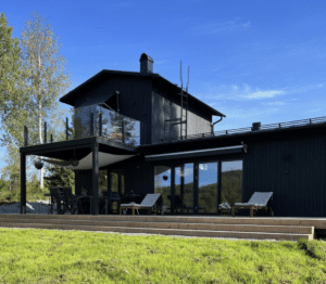 Moderne glasværn med sorte stolper og røgfarvet glas monteret på øvre træterrasse ved sort facade.