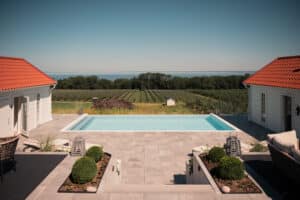 Stolpefrit glashegn med udsigt over hav og landskab Moderne stolpefrit glashegn omkring infinitypool med udsigt over hav, æbleplantage og åbent landskab.