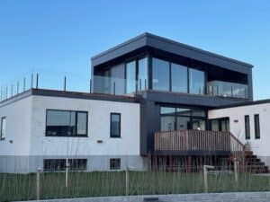 Stolpefrit glasværn rundt om tagterrasse på moderne villa med store vinduer og minimalistisk facade.