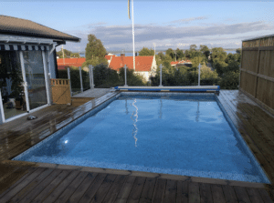 Glashegn omkring pool i villahave Glasrækværk i hvid aluminium monteret omkring hævet villapool med træterrasse og havudsigt – stilrent og børnesikret.