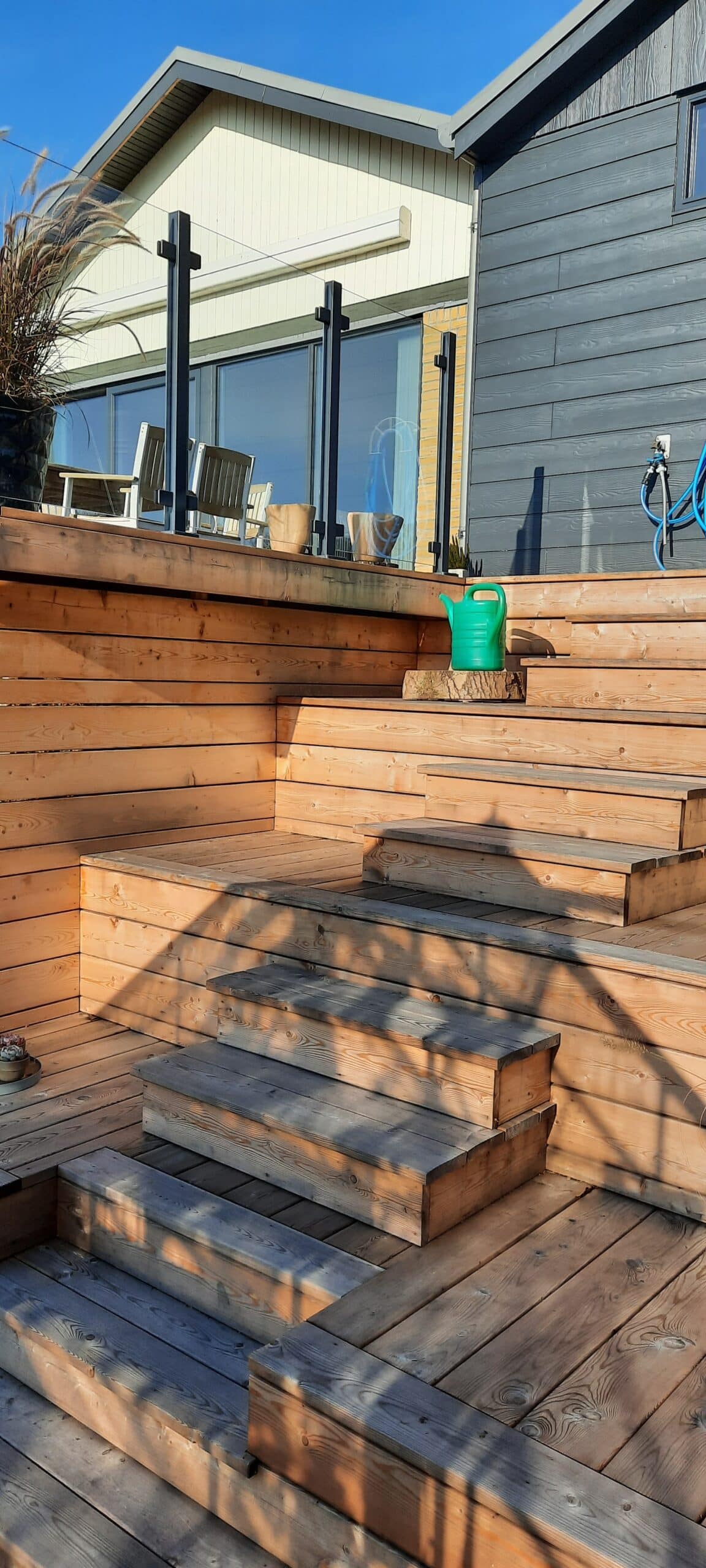 Trappe i træ op til terrasse med glasrækværk i sort aluminium foran facade i to farver.