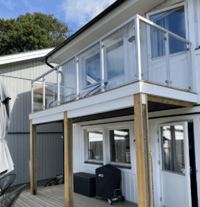 Glasværn med hvide aluminiumstolper monteret på altan med trædæk og facade i naturtræ.