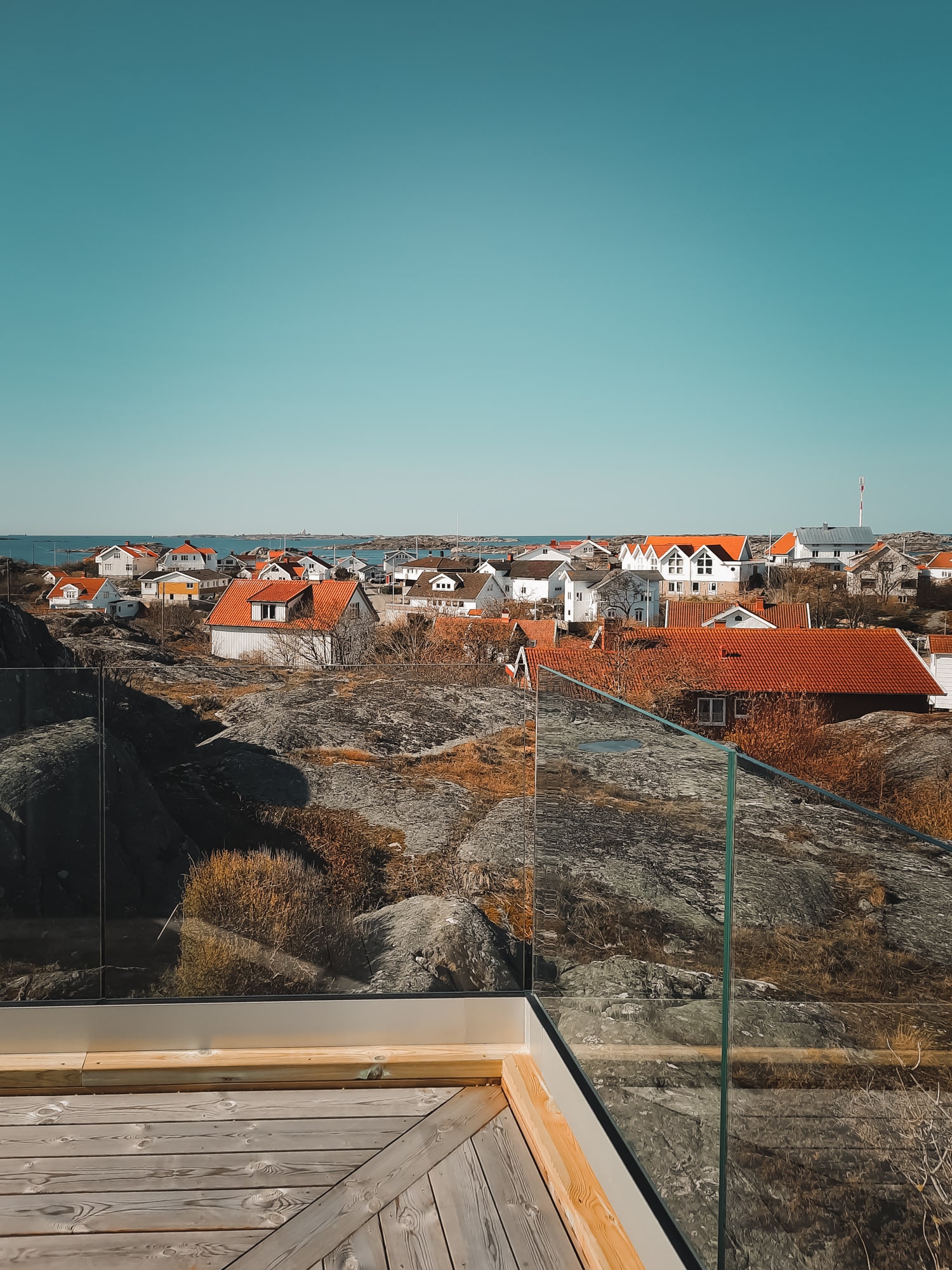 Glasgelænder uden stolper på tagterrasse med panoramaudsigt over kystby og klipper.